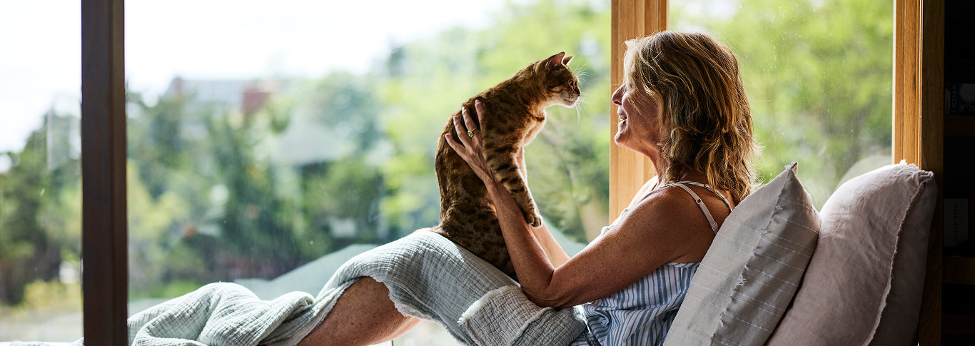 Donna Lennard lounges in a window nook at home while holding her cat.